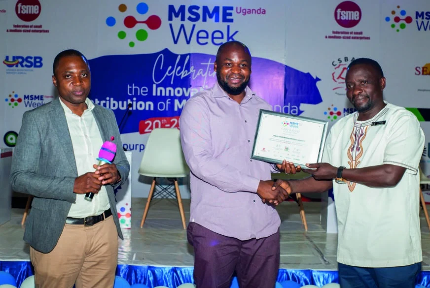 A participant holds a framed certificate and shakes hands with a presenter on stage.