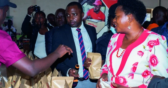 An exhibitor discusses packaged products with visitors at an exhibition stand.