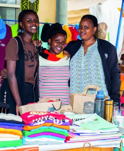 Three exhibitors stand together behind a display of clothing, printed materials and merchandise.