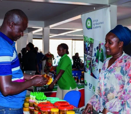 An exhibitor discusses jars and bottles of products with a visitor.